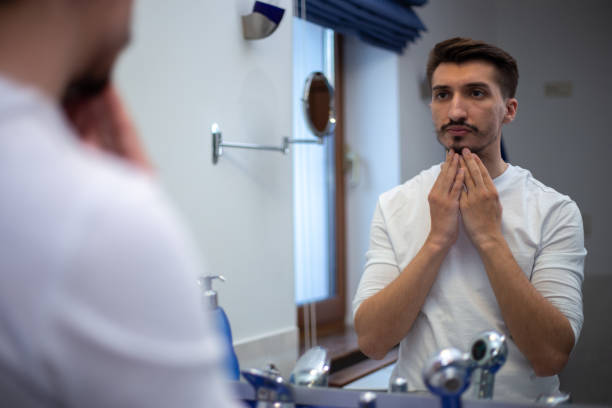 istock A guy with a patchy beard looks in the mirror 1355702859