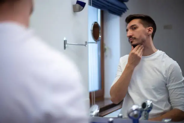 Photo of A guy with a patchy beard looks in the mirror