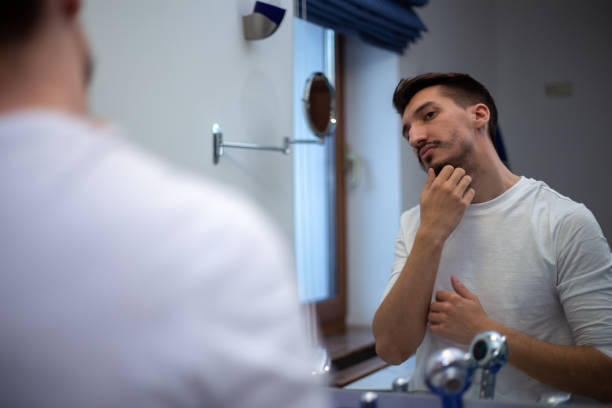 istock A guy with a patchy beard looks in the mirror 1355702923