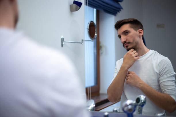 istock A guy with a patchy beard looks in the mirror 1355702925