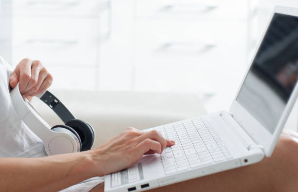 femme assise sur un canapé tapant sur un ordinateur portable avec des écouteurs, rencontres - typewriter key audio photos et images de collection