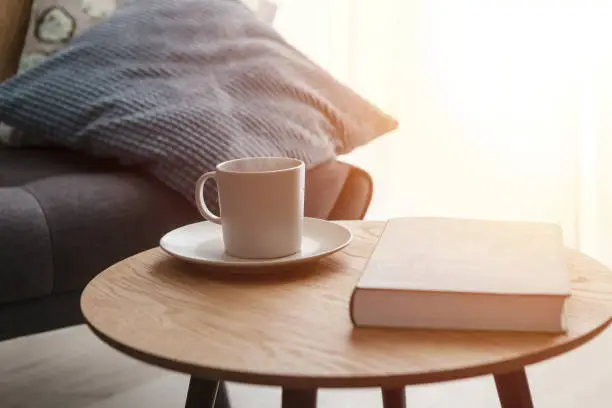 Photo of Relax at home, cup of hot tea and book on coffee table by the sofa