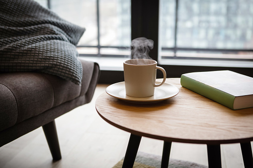 Relax at home, cup of hot tea and book on coffee table by the sofa