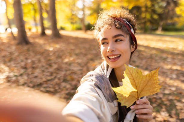 istock Smiling woman taking selfie in park while holding leaf 1355705620