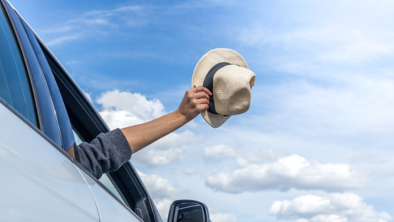 Woman's hand pulls a hat out of a car window. Freedom, travel and vacation concept.