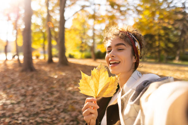 istock Smiling woman taking selfie in park while holding leaf 1355706517