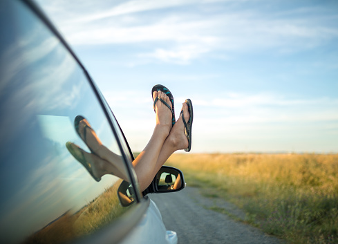 Girl sticking her feet in flip flops out of a car window.
