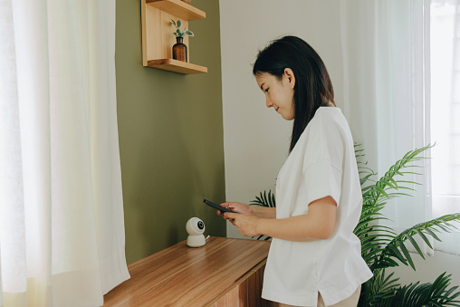 Young woman using smart phone with launched security application and IP camera at the table. Home video surveillance concept