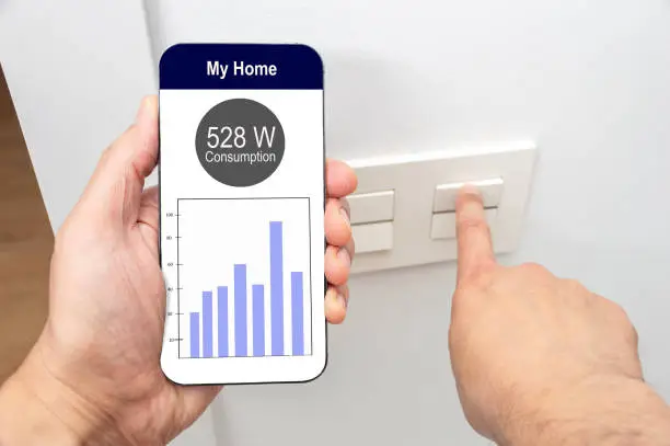 Photo of man hand turning on the light with phone and the display of a smart electric meter