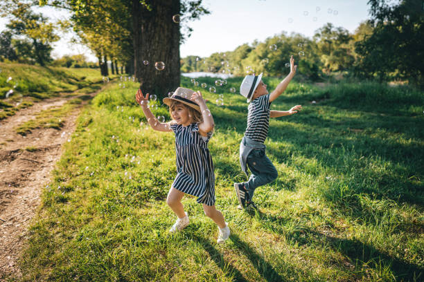 istock Brother and sister chasing soap bubbles in nature 1355713936