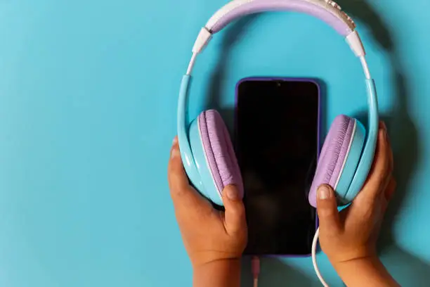 Female hands holding a modern smartphone and headphones on a pastel background. Sync gadgets, interaction. Top view