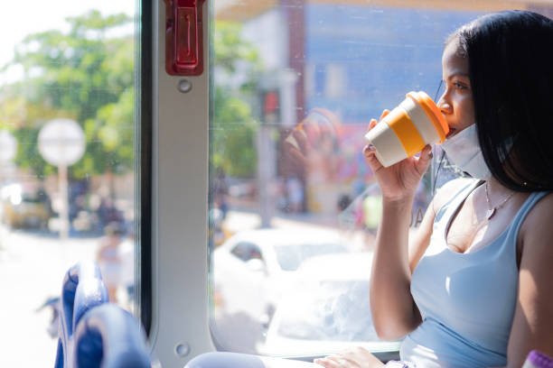 パンデミック中にバスに乗っている間にコーヒーを飲む女性 - african mask ストックフォトと画像