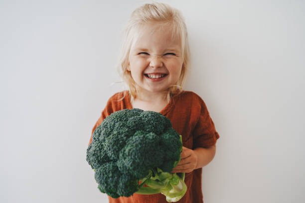 child girl with broccoli healthy food vegan eating lifestyle organic vegetables plant based diet nutrition funny kid happy smiling - healthy lifestyle vegetable food organic imagens e fotografias de stock