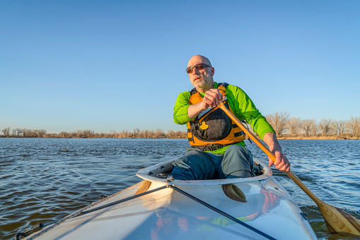 senior male is paddling expedition canoe with a wooden paddle, spring or fall scenery on a lake in northern Colorado, POV from boat bow