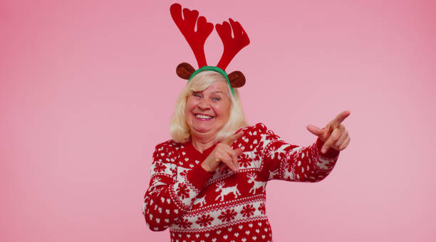Crazy senior elderly grandmother woman demonstrating tongue out, fooling around making silly faces Little bit crazy. Funny mature grandmother woman in Christmas sweater, hat demonstrating tongue out making silly faces fooling around having fun isolated on pink background. Happy New Year celebration christmas sweater photos stock pictures, royalty-free photos & images