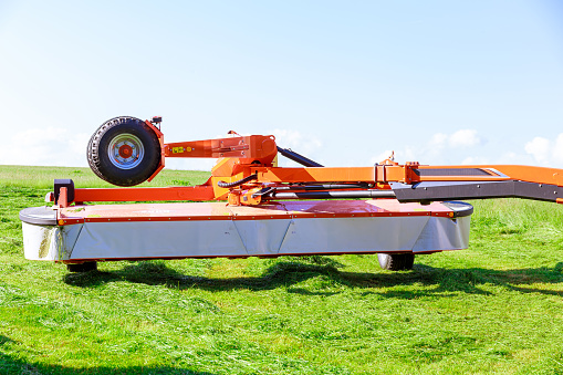 A red rotary mower cut the grass in the field. Clear field. Drying hay in the field.