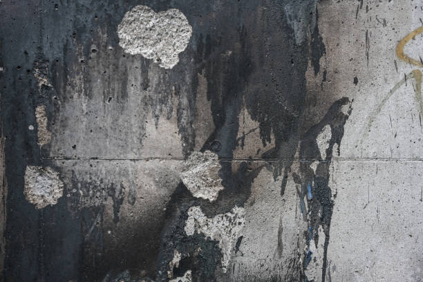 Background texture of a soiled and cracked gray concrete wall with dark paint and fire residue, concept for social issues or down town architecture themes, copy space stock photo