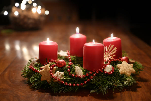 Fourth Advent - decorated Advent wreath from fir branches with red burning candles on a wooden table in the time before Christmas, festive bokeh in the warm dark background, copy space, selected focus stock photo