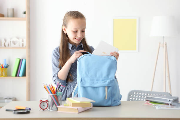 istock Cute cheerful schoolgirl puts stationery in a backpack. 1355738367