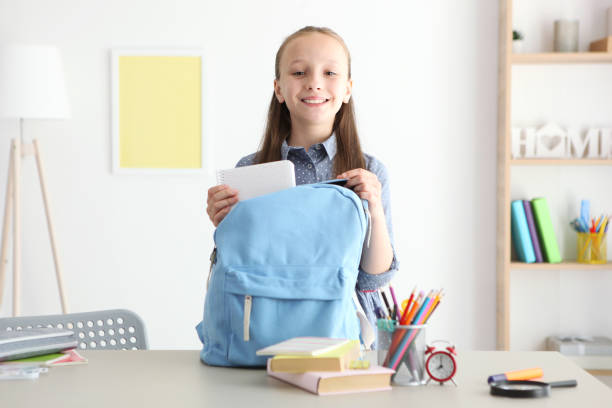 istock Cute cheerful schoolgirl puts stationery in a backpack. 1355739726