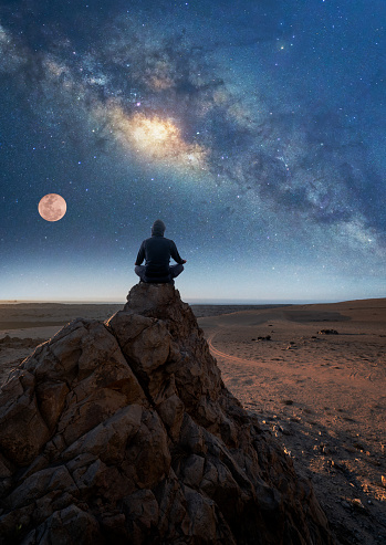 person sitting on the top of the mountain meditating or contemplating the starry night with Milky Way and Moon background in Atacama Desert