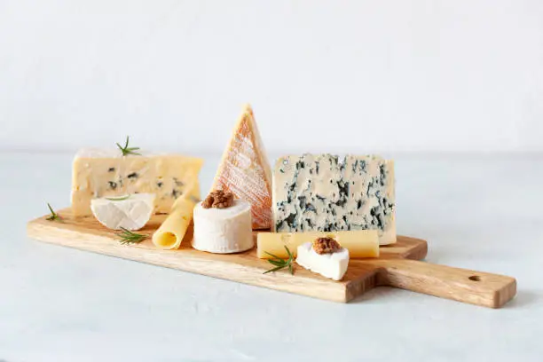 Different types of cheese on a cutting board on white background