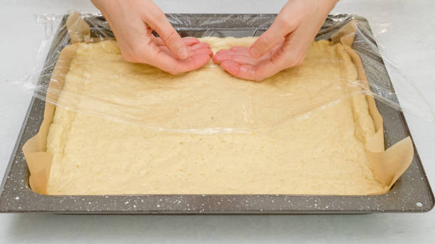 istock Woman's hands using plastic wrap unfurl pizza dough onto prepared baking pan. Homemade pizza step by step recipe 1355758516