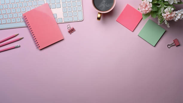 istock Female workplace with notebook, coffee cup and sticky notes on pink background. 1355771427