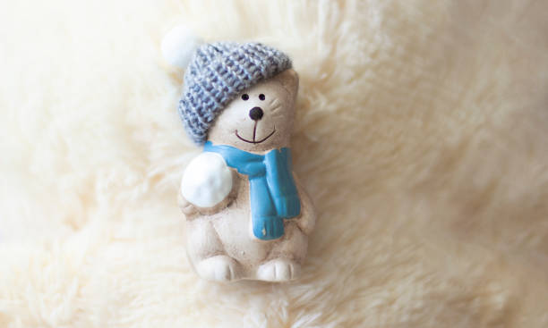 istock Ceramic teddy bear in a cap on a white fluffy background. 1355775769