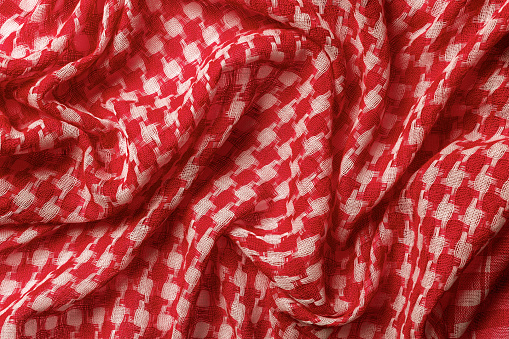 Draped shemagh of red white colors background. Arab desert scarf hirbawi texture. Folded cotton keffiyeh macro. Full frame kefia pattern. Traditional Middle East head scarf kufiya. Top view.