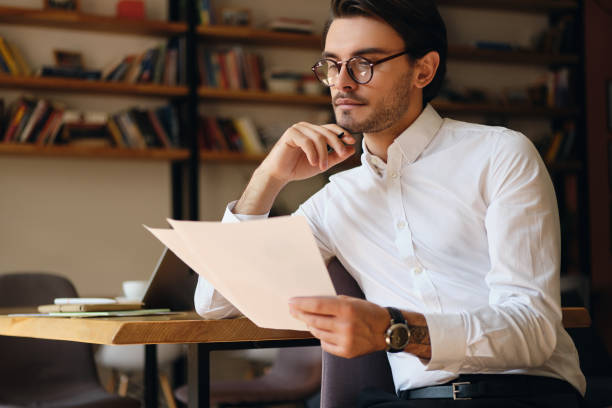 istock Young handsome businessman in eyeglasses dreamily working with papers in modern office 1355784792