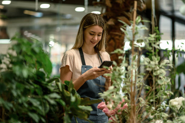 istock Florist using smartphone while surrounded with flowers and plants in a flower shop 1355785703
