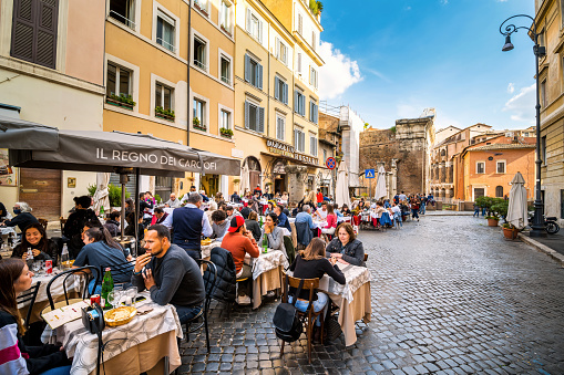 Rome, Italy, October 16 -- Dozens of tourists and customers enjoy life and Italian cuisine in the open-air restaurants along Portico d'Ottavia street in the heart of Rome's Jewish Ghetto. The iconic Jewish Quarter of Rome, the oldest ghetto in Europe, is famous for the presence of hidden alleys and small squares, where it is easy to find small restaurants of Italian and Jewish cuisine, and remarkable Roman archaeological remains. The ghetto of Rome is located in one of the oldest districts of the city between the Campidoglio (Roman Capitol) and the River Tiber. In 1980 the historic center of Rome was declared a World Heritage Site by Unesco. Super wide angle and high definition image.