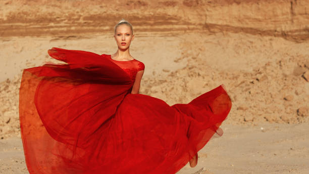 Người mẫu nữ tóc vàng gợi cảm trong chiếc váy đỏ xinh đẹp thanh lịch nằm trên cát.