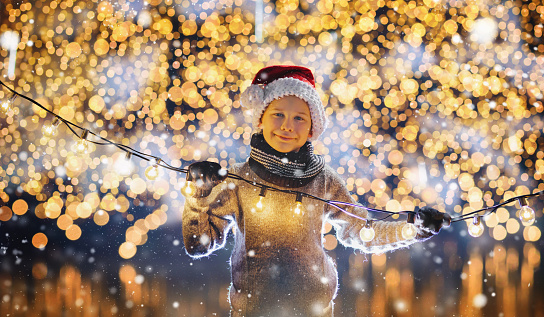 a happy boy at christmas with fairy lights in the snow