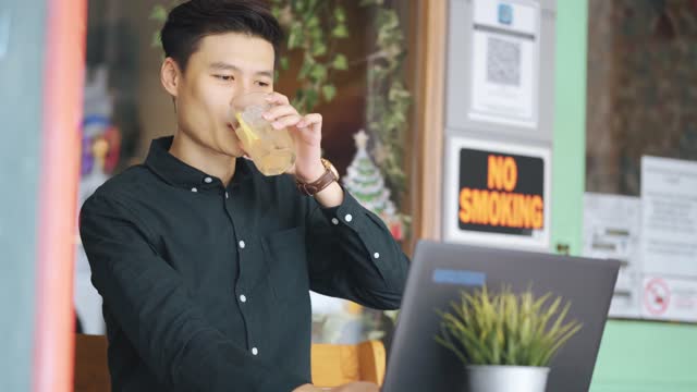 Smiling professional young Asian chinese businessman working using laptop at cafe patio outdoor