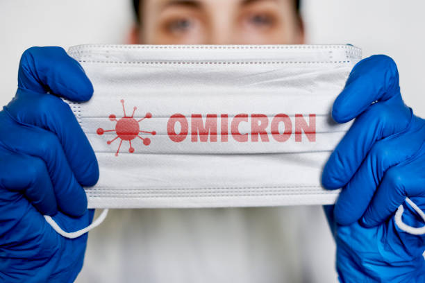 Covid-19 new variant - Omicron Female doctor holds a face mask with - Omicron variant text on it. Covid-19 new variant - Omicron. Omicron variant of coronavirus. SARS-CoV-2 variant of concern world health organization photos stock pictures, royalty-free photos & images