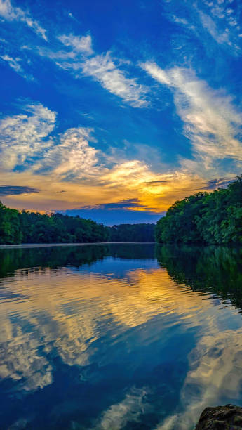 Sunrise on a partly cloudy day over tree-lined lake with reflection in the water stock photo