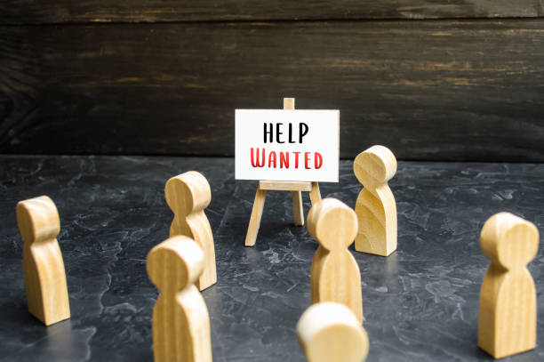 istock A man with a Help Wanted sign appeals to the crowd about hiring. Call for help, volunteering. Search and recruitment of new employees for work. Hire staff. Employment Agency. Recruiting, staffing. 1355811408