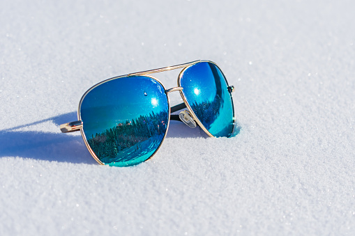 Sunglasses with blue lenses in which the forest is reflected lie on the snow