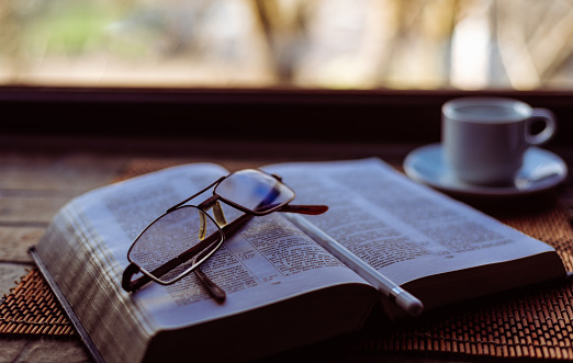 Bible In Russian Language With Reading Glasses And  Ceramic Cup A Coffee On Window Seal Close Up