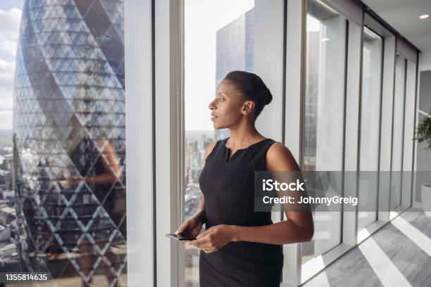 Contemplative British Businesswoman Standing At Window Stock Photo - Download Image Now