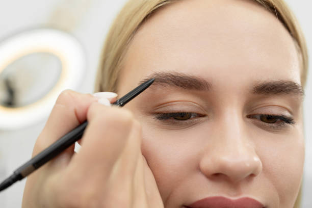 istock Stylist draws eyebrows with a pencil for a young beautiful woman. 1355816908
