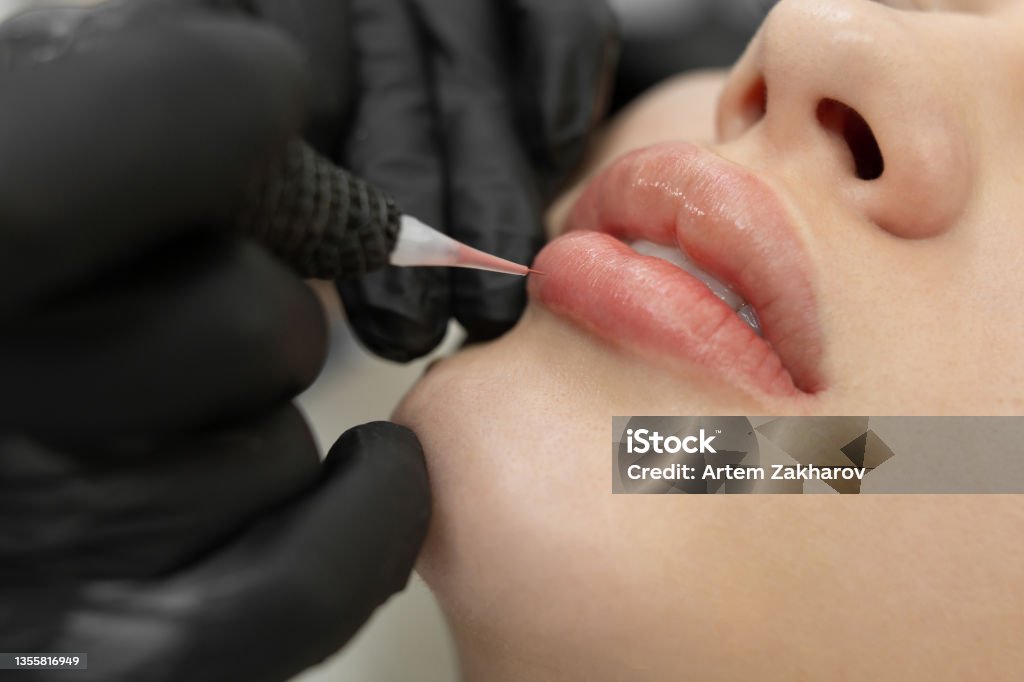 Close-up of the permanent makeup procedure. Lip makeup in the cosmetologist's salon. Human Lips Stock Photo