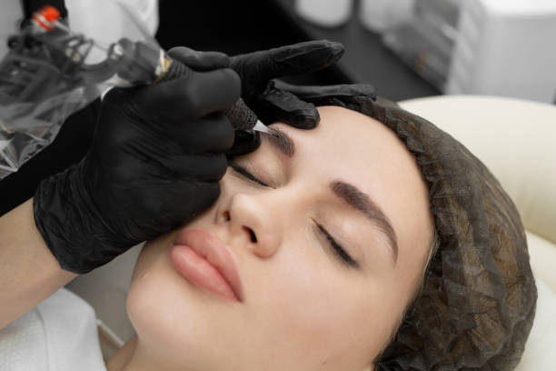istock Concept of microblading eyebrows. The cosmetologist performs the procedure of permanent makeup of the eyebrows in close-up. 1355816960