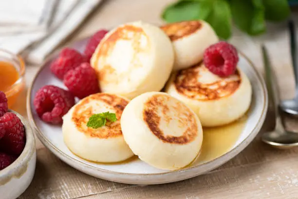 Cheese fritters Syrniki with raspberries and honey on a plate. Russian, Ukrainian cuisine food. Sweet cheese pancakes