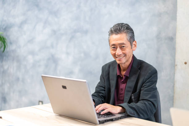 un homme âgé utilisant un ordinateur - laptop japanese ethnicity businessman desk photos et images de collection