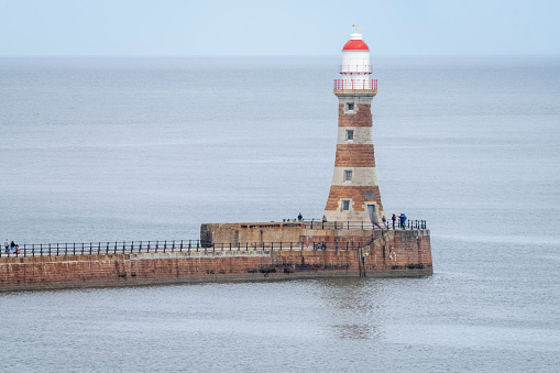 People walking along Roker Pier on a bright summer day towards the Lighthouse at the end.  Roker Pier is on the North Sea Coast at Sunderland, Tyne and Wear, England, UK.