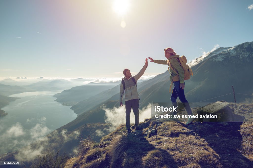 Personal perspective of Two hikers celebrating on mountain top with a high five Two hikers celebrating on mountain trail with a high five. Shot in Switzerland, Springtime. Mountain Climbing Stock Photo