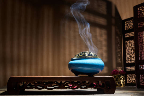Smoke from burning incense sticks standing on lotus incense holder.